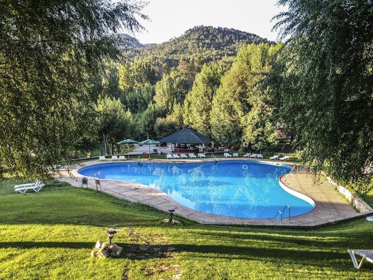Relax at a luxury resort pool surrounded by lush greenery and scenic hills in Jaén, Spain.